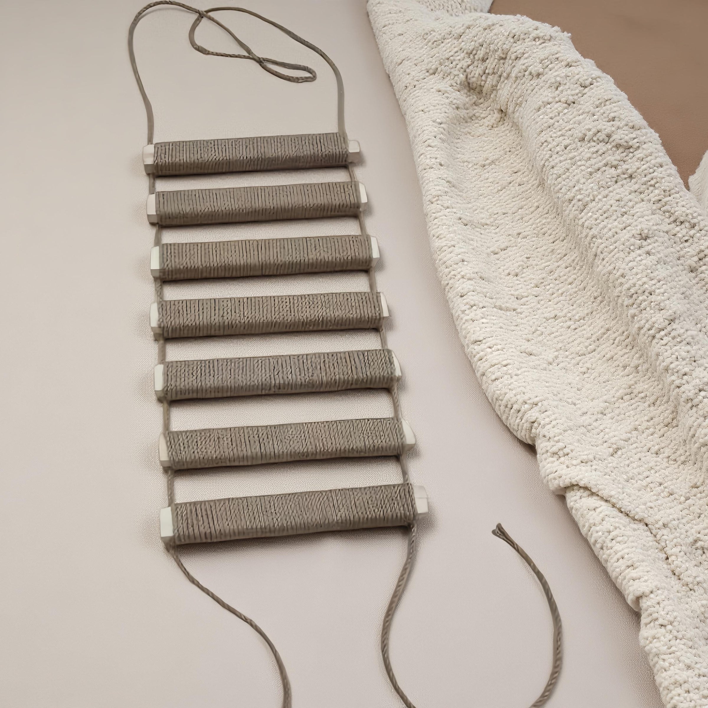 Natural-tone cat climbing rope ladder laid flat beside a cream textured blanket